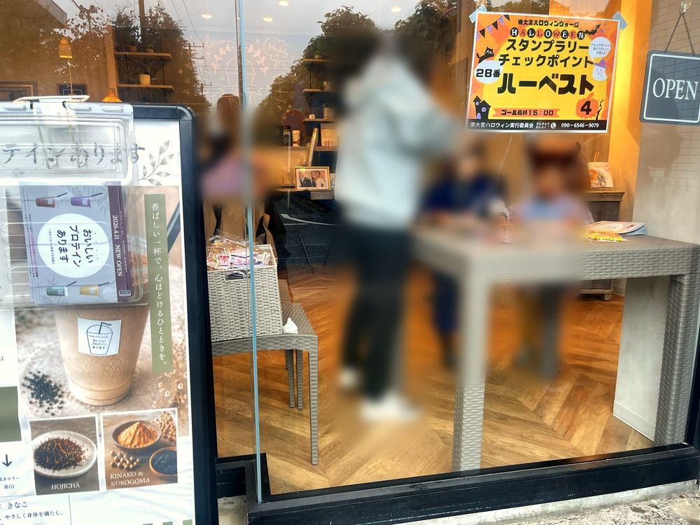 おいしいプロテインハーベストの店先。窓にスタンプラリーのチェックポイントの案内