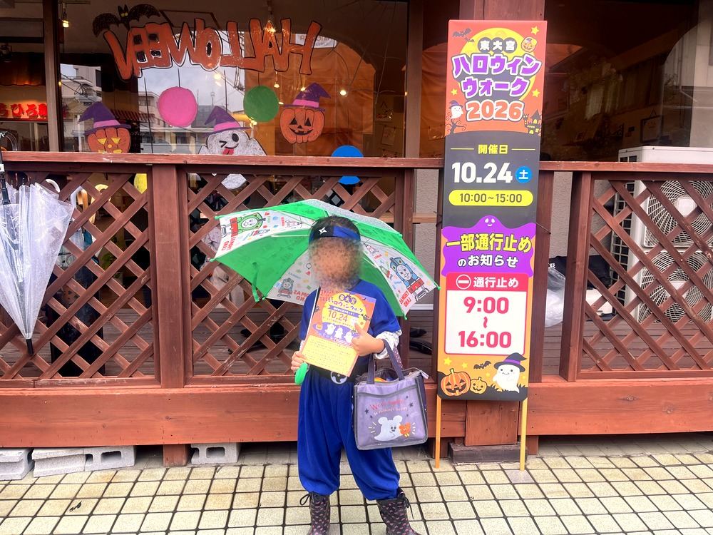 ちひろ珈琲の前に立つ東大宮ハロウィンウォーク2026ののぼりと、ニンジャの仮装の子ども。のぼりには開催日10月24日と一部通行止め9時から16時の案内