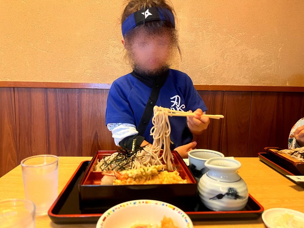 スタンプラリーの途中、そば処山茂登でおそばを食べるニンジャの仮装の子ども