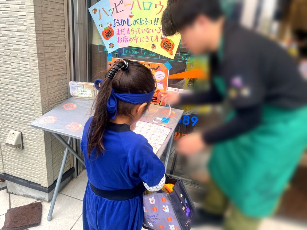 お店の前の机で、店員さんにスタンプラリーカードへスタンプを押してもらう子ども