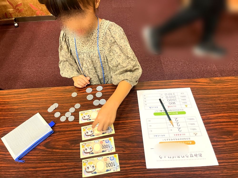おもちゃのお金を数えて売上を計算する5歳の子ども(顔はぼかし)