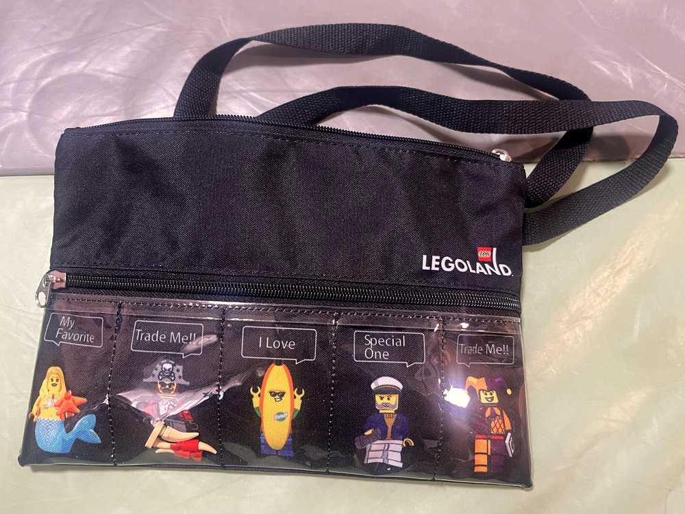 前のクリアポケットに「Trade Me!」の吹き出しとミニフィグが入った、LEGOLANDのロゴ入りの黒いバッグ