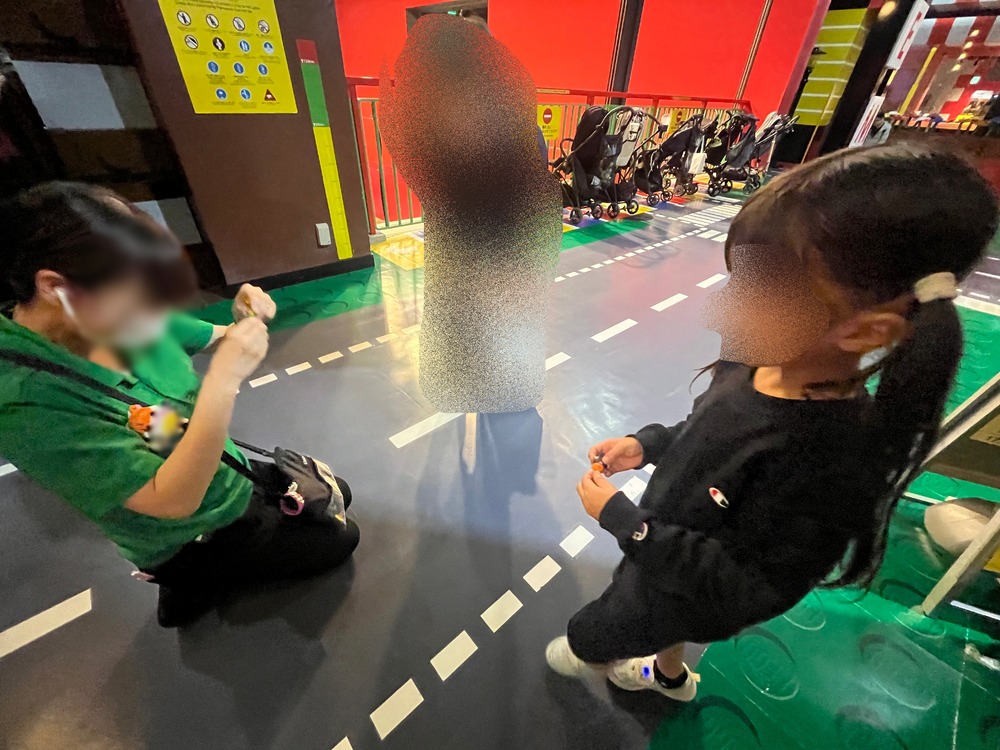 しゃがんだスタッフさんとミニフィグを交換する子がめ(顔はぼかし)
