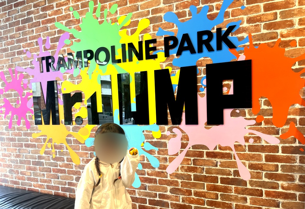 Mr.JUMP松戸店の入口のロゴ壁の前に立つ子ども