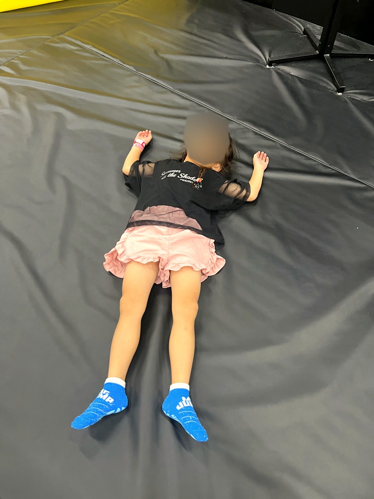 遊び疲れてトランポリンの床に寝転がる子ども