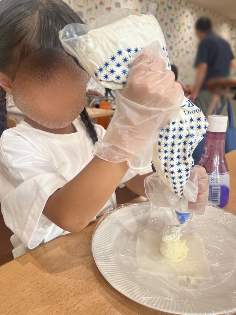 大福の皮にアイスとクリームをのせる子ども