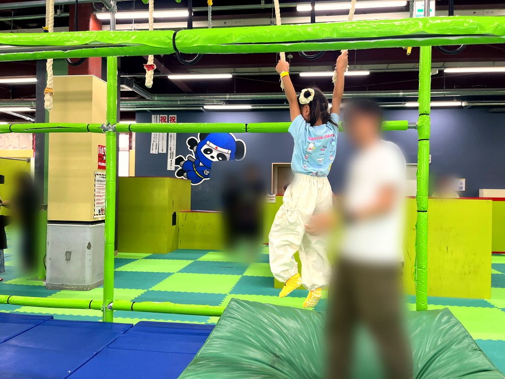 ニンジャスロンのロープのうんていにぶら下がる5歳の子どもと、そばで見守る大人