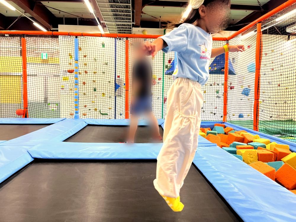 トランポリンで跳ぶ5歳の子ども。奥にはスポンジプール